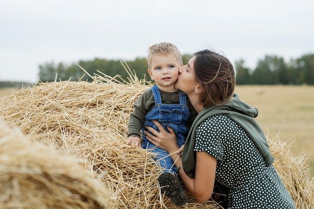 A young woman kissing her child on the cheek in front of hay.